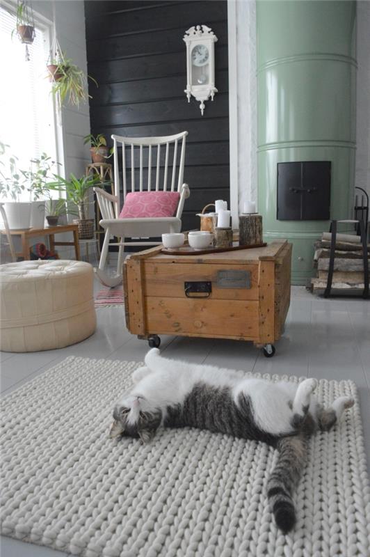 öppen spis hörn hygge deco spirit med ett återvunnet soffbord i trä, en gungstol och en läderpuff, en söt katt som ligger på en grå stickad matta framför spisen