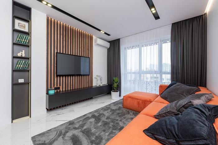 sivý koberec obývacia izba deco oranžová rohová sedačka dlhé tmavé záclony biela stena led osvetlenie čierny nábytok