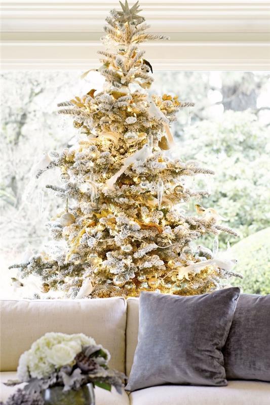trendig julinredning 2019, vardagsrum med stort fönster möblerat med beige soffa och julgran i guld och silver