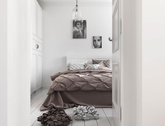 Škandinávsky model spálne, hnedá posteľná bielizeň, biela posteľ, biele parkety, nástenné dekorácie s grafickými portrétmi