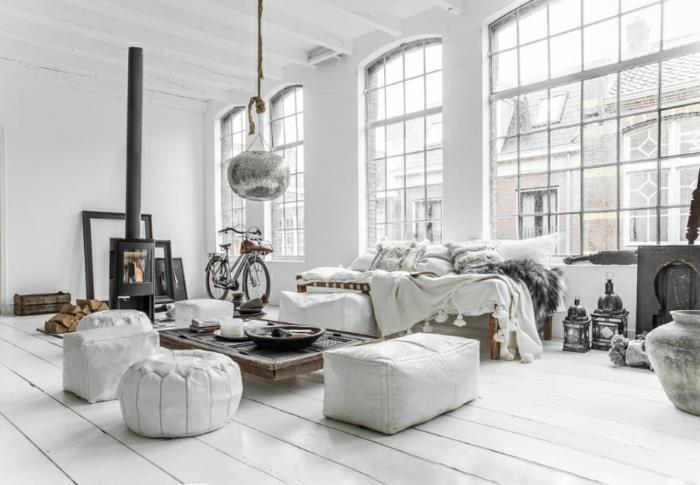 Škandinávsky dekor v obývacej izbe v bielej farbe, biele parkety, biela sedačka so sivou pokožkou, zaujímavý dizajnový konferenčný stolík, sivé pufy, bielené parkety, krb, originálne závesné svetlo, ozdobné lampáše