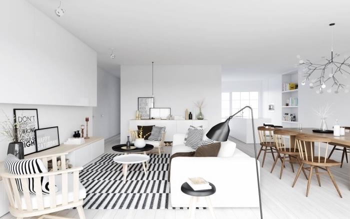 Škandinávske usporiadanie obývačky otvorené do jedálne, čiernobiely koberec, biela pohovka, drevené stoličky, svetlé parkety, stoličky do jedálne a drevený stôl