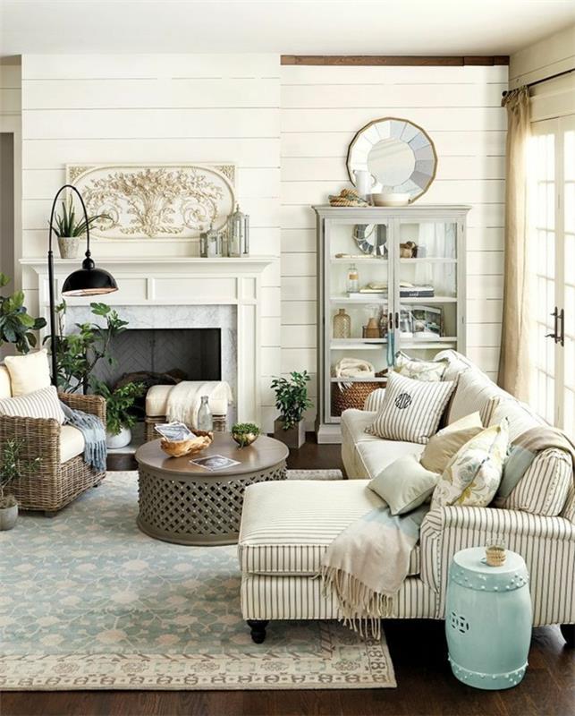 rustik stil deco, blommönstrad matta, randig soffa och rottingfåtölj, runda orientaliska soffbord, öppen spis, vintage vit skänk, brun parkett, country chic inredning