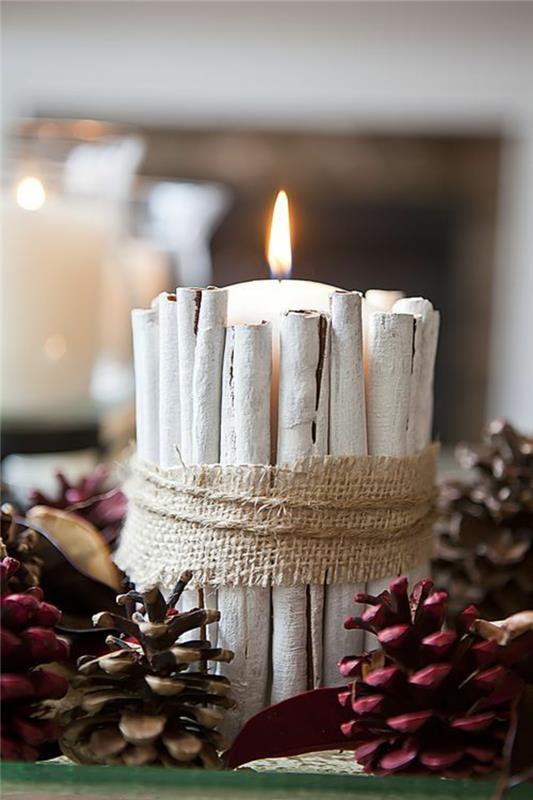 Vianočná dekorácia, aby ste si to uľahčili, veľká biela sviečka so škoricovými tyčinkami pomaľovaná bielou farbou, šišky zafarbené na červeno, vianočný stredobod