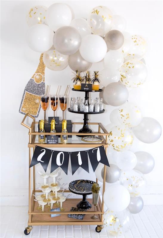 båge av vita och guldballonger runt en guldfärgad skänk med originella dekorativa accenter, glasögon, flaskor champagne