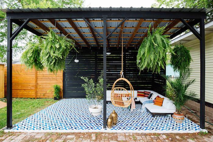 utomhusterrass i deco, blått och vitt mosaiköverdrag, hängande gunga, träsoffa, vit sittdyna och färgglada dekorativa kuddar, hängande gröna växter, modern aluminiumpergola