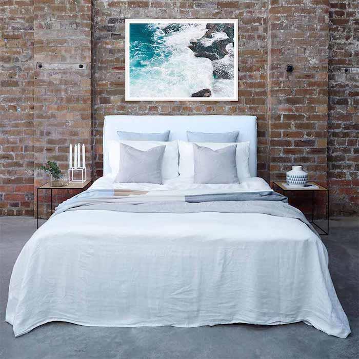 havslandskap fotoram huvudgavel modell med vita och gråa sängkläder, tegelvägg bakom sängen, industriell stil deco