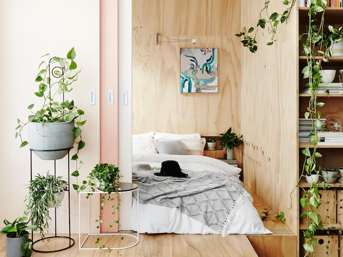 drevená podlahová a stenová krytina, podlahový matrac so sivou a bielou posteľnou bielizňou, izbová závesná rastlina, knižnica s rastlinami a knihami