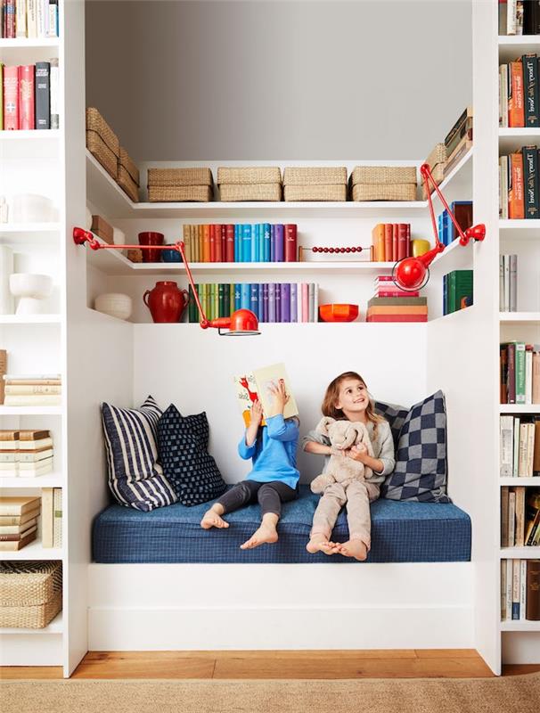 barns läshörna dekoration väggnisch med bänk med blå madrass och kuddar och väggbibliotek med böcker