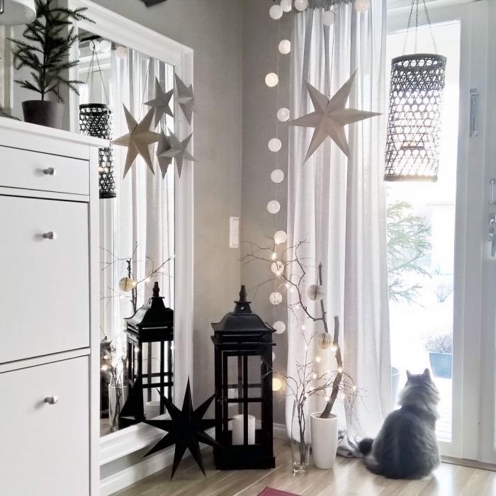 grå och vit vardagsrumsinredning i festlig anda, hörn av vardagsrummet dekorerat med dekorativa lyktor, hängande pappersstjärnor och en vacker krans av ljusa bollar