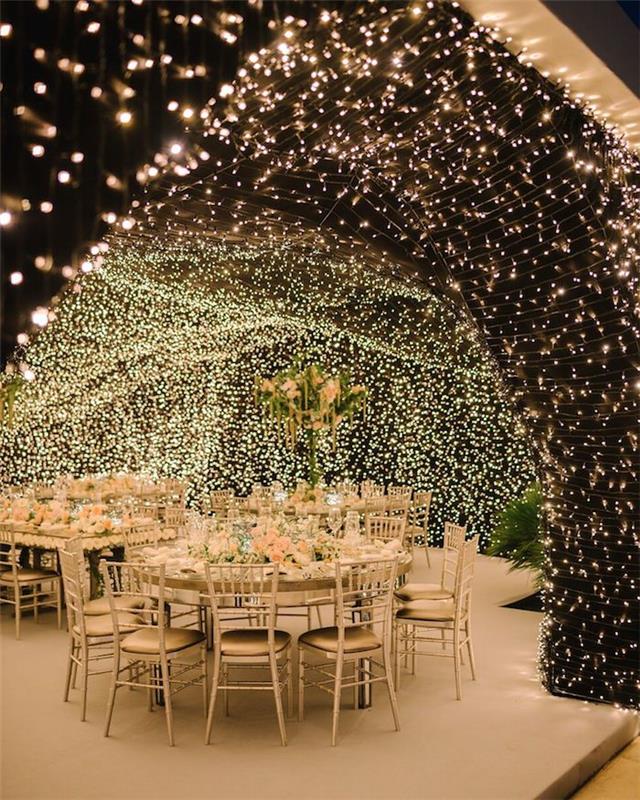 príklad dekorácie svadobného stropu vo vegetačnej pene a svetlých girlandách, niekoľko svetiel nad stolmi v elegantnej bielej a zlatej svadbe