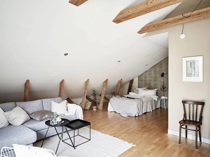 synliga takbjälkar i ett vindrum med sluttande säng och grå soffa, svarta häckbord, grå och vita väggar