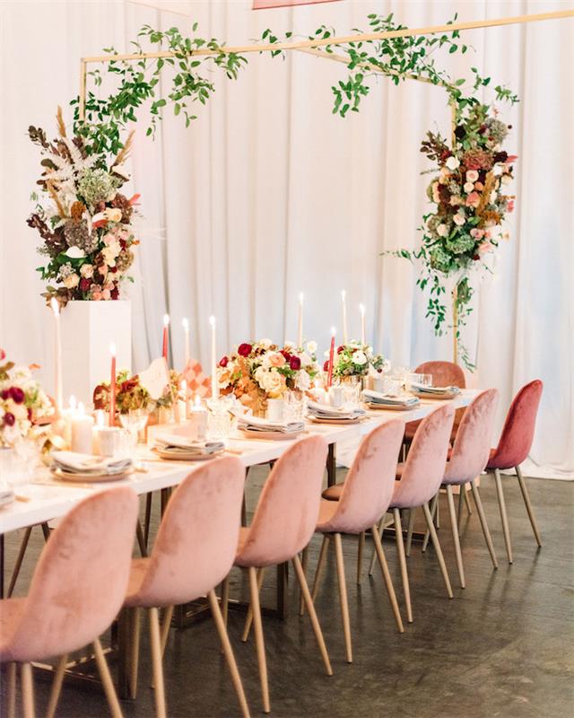 ružové rady stoličiek okolo bieleho stola, bohémsky elegantný svadobný dekor s bohatými kvetinovými aranžmánmi, dekoratívny dekor sviečok