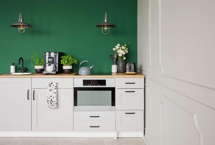 نموذج لمطبخ صغير مجهز بطول مقطع من الجدار مطلي باللون الأخضر الداكن مع أثاث أبيض وطاولات خشبية