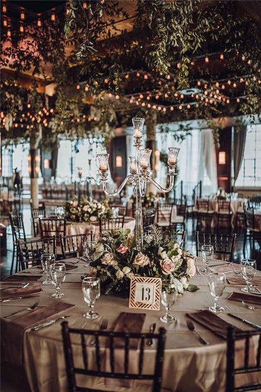 stredobod svadby so zelenou vegetáciou a ružovými kvetmi, zelený strop osvetlený svetelnými girlandami, sklenené svietniky, romantický nápad na svadobné deko