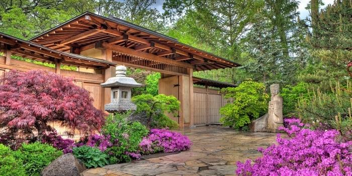 المدخل قوس ياباني ، فضاء ، مغطى بألواح حجرية ، محاط بالنباتات الخضراء والزهور ، فانوس وتمثال ياباني