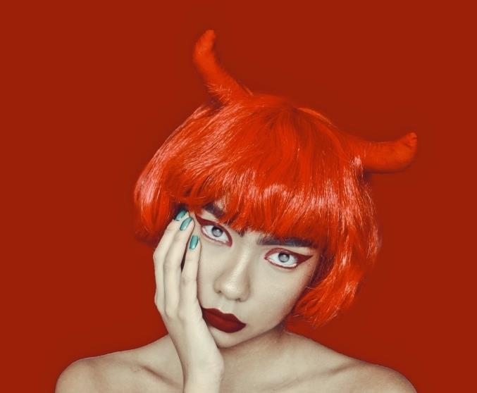 djävulssmink med matt röd mun och en blick framhävd av färgglad eyeliner, framgångsrik djävul förklädning röd fyrkantig peruk med lugg och djävulshorn