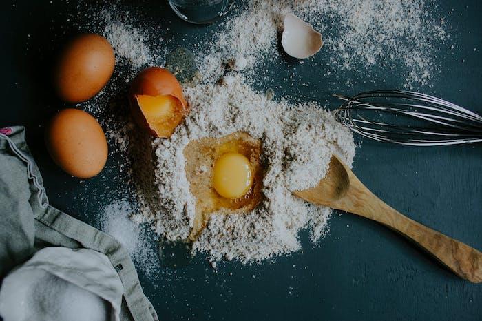 rozbité vajíčka v kope múky na pulte vedľa šľahača a varešky varenia doma