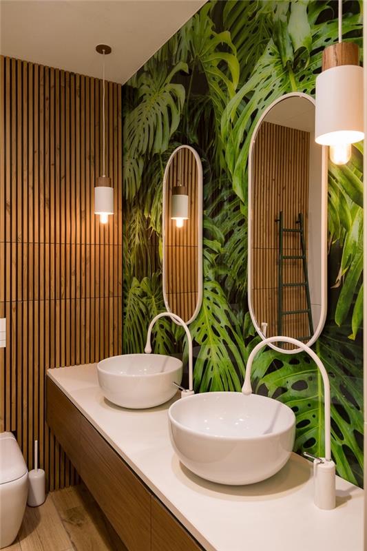 toaleta v tropickom štýle s tapetou trompe l'oeil s listami monstera a dreveným obložením, drevená a biela skrinka na umývadlo
