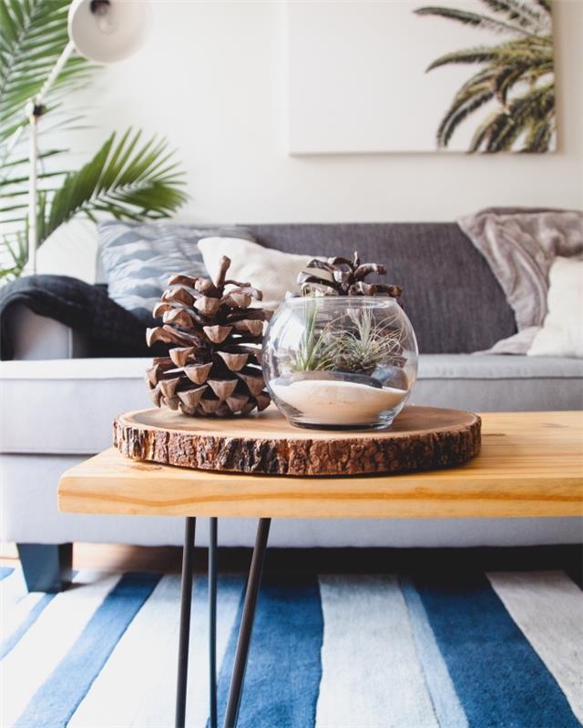 mysig och minimalistisk inredning i ett vardagsrum möblerat med soffa och dekorerat med gröna växter och DIY -föremål, dekorativ tallkotte
