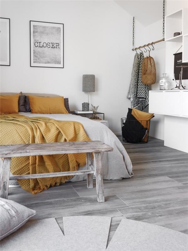 Sovrum i minimalistisk stil med vita väggar och ljusgrå parkett, sängkläder och dekorativa kuddar i senapsgul färg