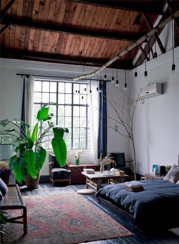 säng med grått sänglinne, vita väggar, synligt tak i träram, orientalisk matta och sittgrupp bredvid, hängande glödlampor