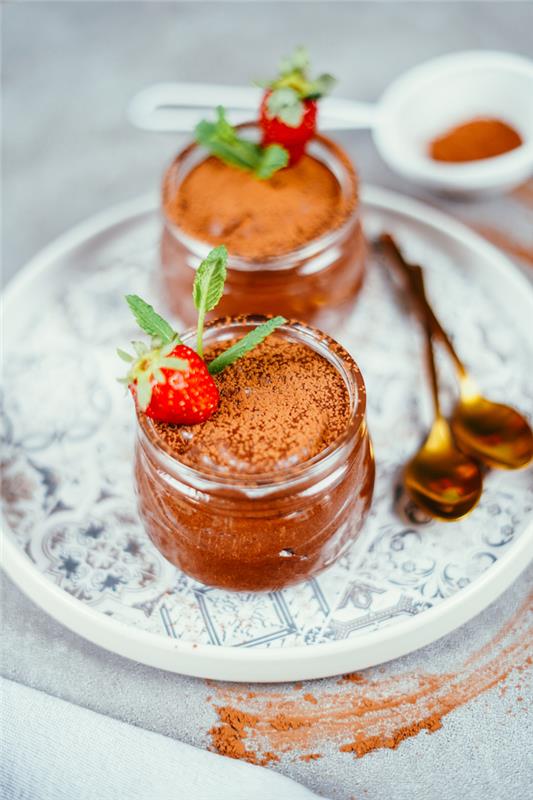 glasburkar fyllda med hemlagad chokladmousse med mörk choklad och aquafaba och dekoration av kakaopulver, jordgubbe, mynta