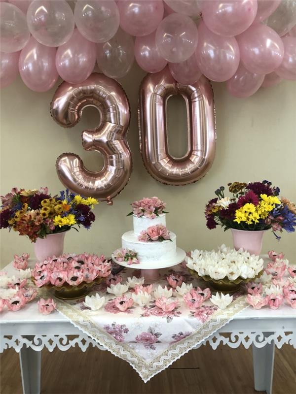 vuxen födelsedagsdekoration i nyanser av rosa och vitt, vitt bord dekorerat med födelsedagstårta och buketter av färska blommor