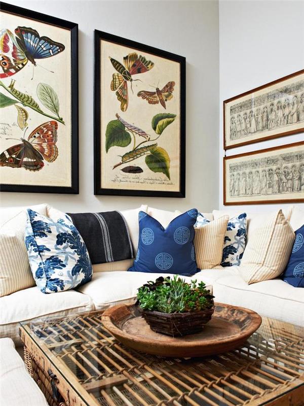 tropiskt tyg, vardagsrum med vita väggar, blå dekorativa kuddar, beige hörnsoffa, grön växt, fjärilsmålning med svarta ramar