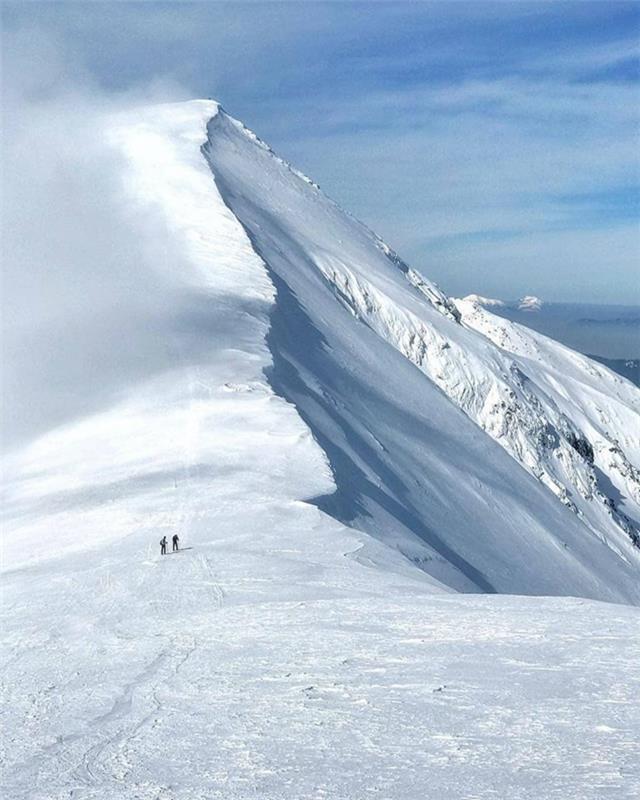 vackert landskap, vackert landskap, berg allt i snö, två människor som går mot det vita toppmötet och en himmel med vita moln som ser ut som en slöja, horisonten halvt synlig bredvid berget