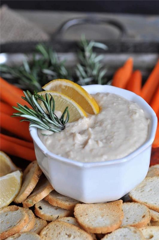 hummus i en vit skål, med citron och rosmarin, enkla veganska aptitretare, bakad bruschetta