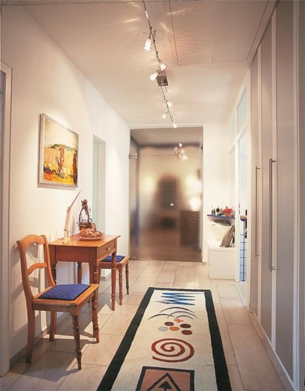 Lång färgstark matta med geometriska mönster, bord och två stolar, smal korridorhylla, konstgjord hallbelysning