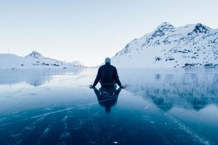 norra landskapet, Alaska, man som sitter på is och stirrar på snötäckta berg framför honom, storblå
