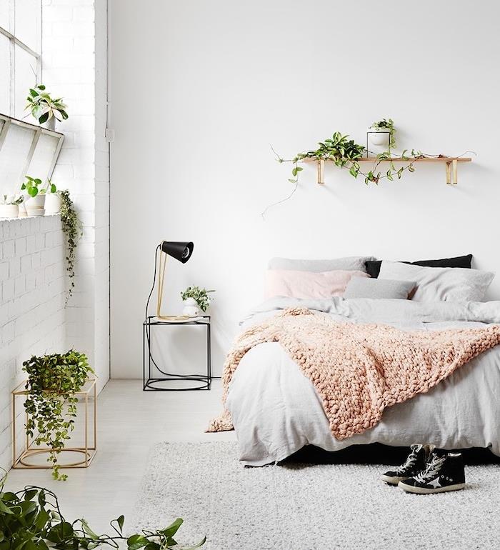 Škandinávska dekorácia spálne so zámotkom so vzorom džungle predstaveným zelenými rastlinami, sivým kobercom, ružovou a sivou posteľnou bielizňou, ružovou, sivou a bielou výzdobou spálne