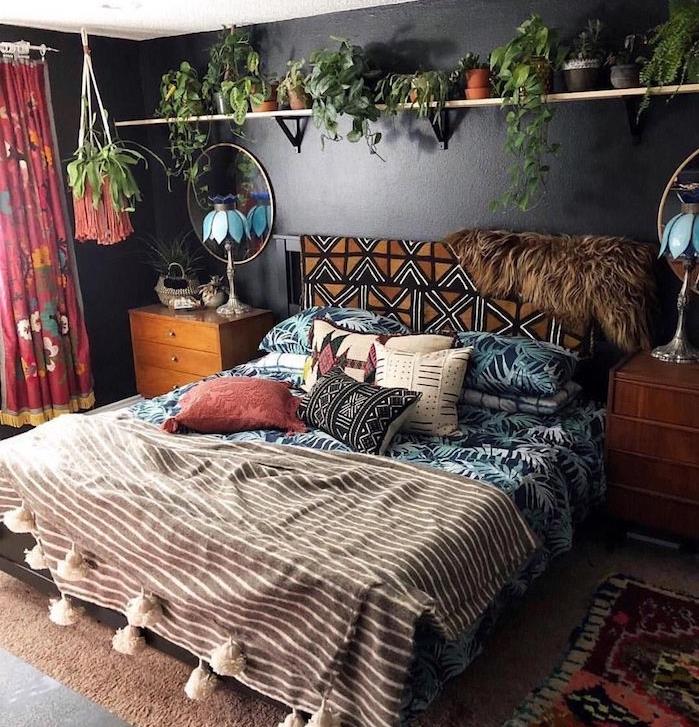 čierna farba steny, tropická a hippie elegantná posteľná bielizeň, hnedý koberec, polica preplnená malými kvetináčmi, vintage komoda, okrúhle zrkadlo, farebné závesy