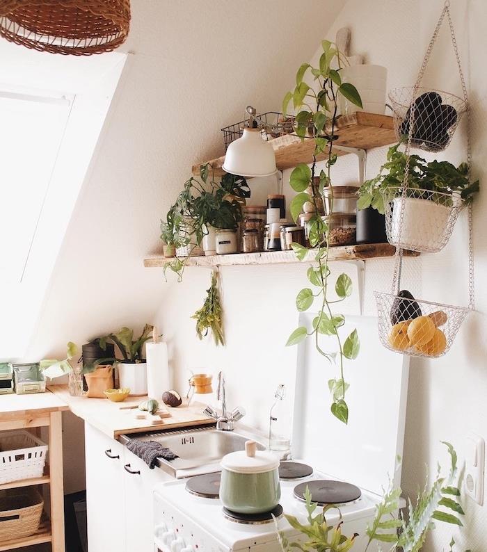 kuchyňa pod svahom, police zo surového dreva zdobené malými rastlinami, bylinkami a prísadami, drevená kuchynská skrinka, biele steny, malé exotické dekoratívne prvky