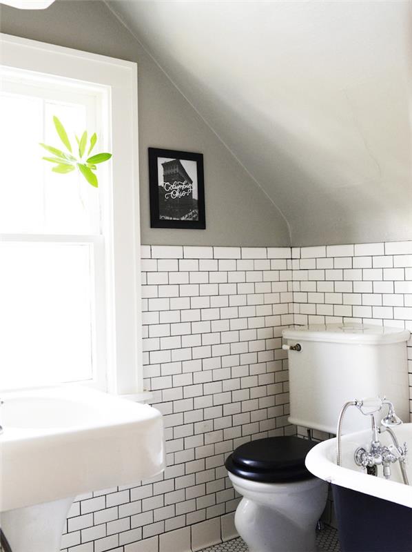 príklad malej kúpeľne, biele obklady metra, šikmý sivý strop, čiernobiela vaňa, biele umývadlo