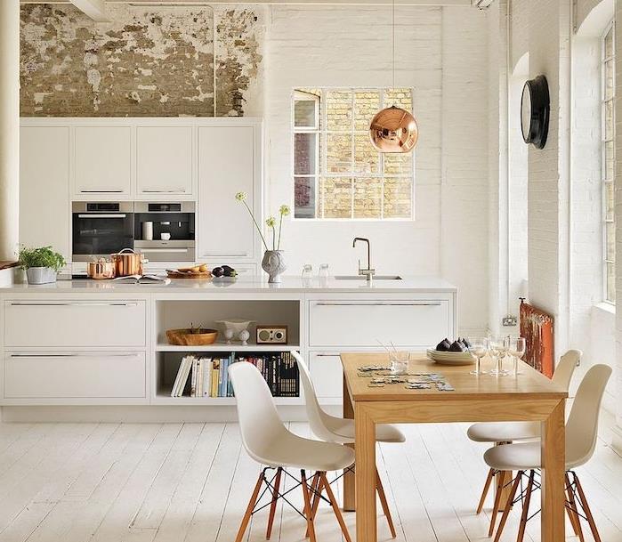 vitlackerat kök med vit bänk, vitkalkat parkettgolv, sittgrupp, träbord och skandinaviska stolar, sliten vägg, kopparlampa
