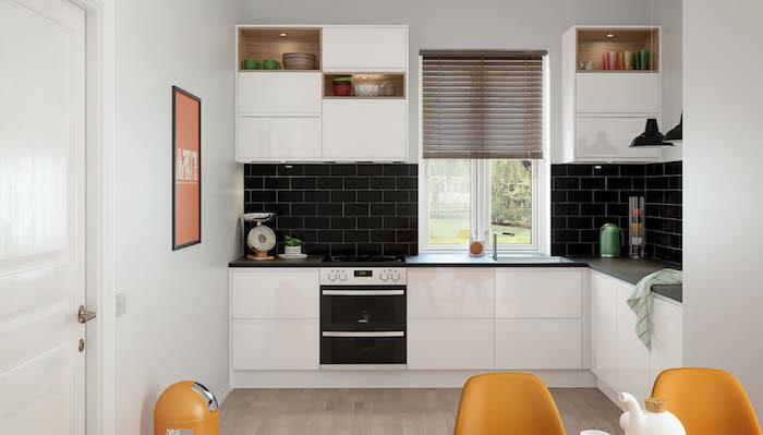 vitt lackerat kök med svart kaklat credecne, trägolv, orange stolar, svart bänkskiva, öppna belysta hyllor