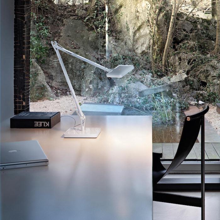 مصباح أبيض مصمم على مكتب اسكندنافي مع كرسي أسود ، فكرة عن نافذة كبيرة تطل على منظر طبيعي ساحر