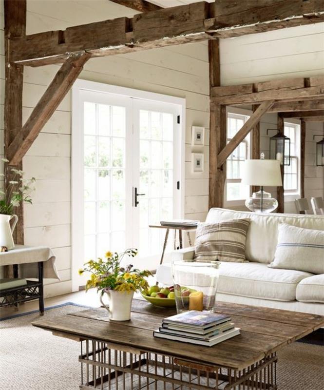 chic rustik lantlig inredning, synlig balk, vit soffa, dekorativa kuddar, brun matta, träplankupphängningsbord och metallkorgfötter