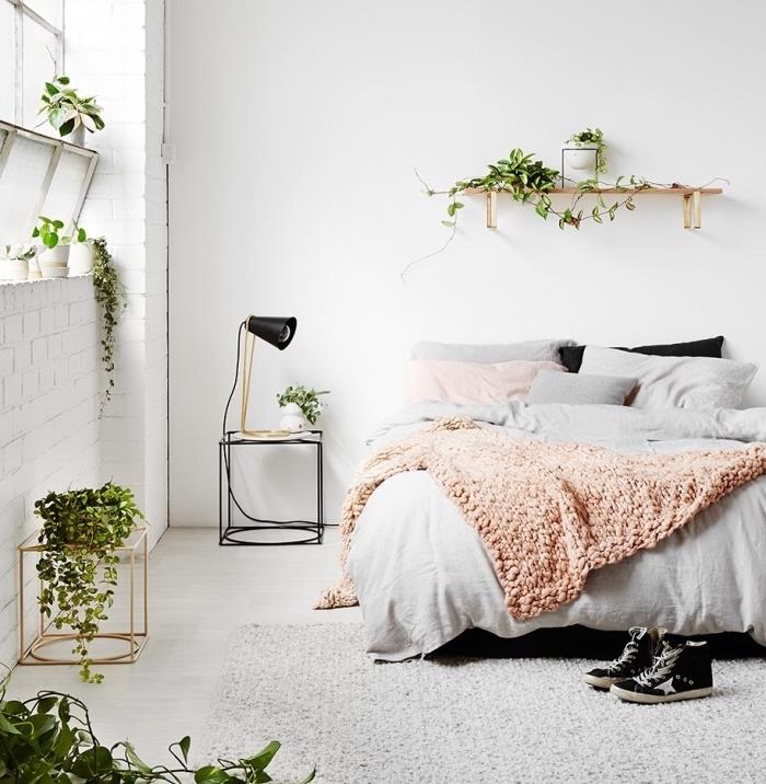 príklad dekorácie inšpirovanej Škandináviou, sivej posteľnej bielizne, prikrývky z lososa, bielych stien a dekorácie rastlín