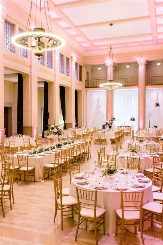 lustre so svetlami nad stolom v bielom obruse a drevených a bielych stoličkách, biele steny, parketová svetlá svadobná miestnosť