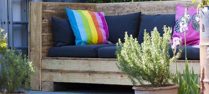 tmavomodrý paletový záhradný vankúš na paletovej lavičke zdobený farebnými dekoratívnymi vankúšmi v záhrade