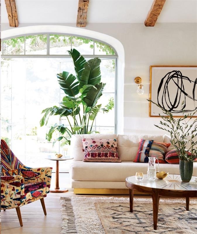 biela obývacia izba zariadená v elegantnom etnickom štýle s exotickými zelenými rastlinami a viacfarebnými vankúšmi s kmeňovými vzormi
