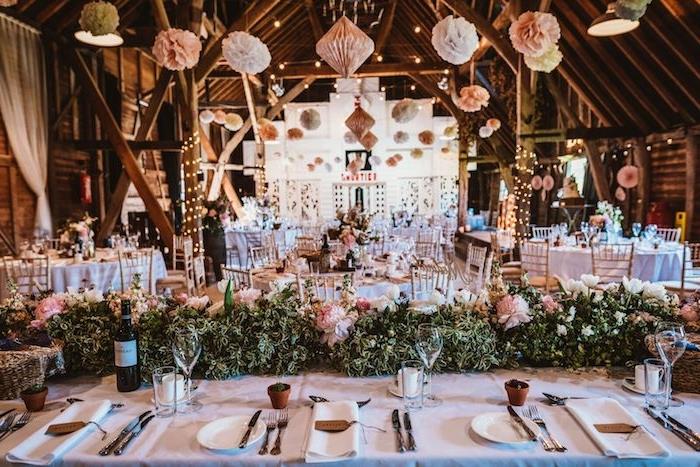 svadobná výzdoba stropu v závesných papierových kvetoch, behúň na stôl s lístím a ružovými kvetmi na bielom obruse, nápadná svadobná téma v stodolách