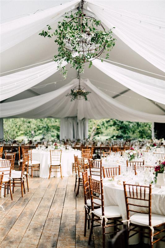 závesný strop s natiahnutými bielymi plachtami, závesné svetlo nad stolmi zo zeleného glóbusu zdobené bielymi obrusmi s bielymi a drevenými stoličkami, parkety zo surového dreva
