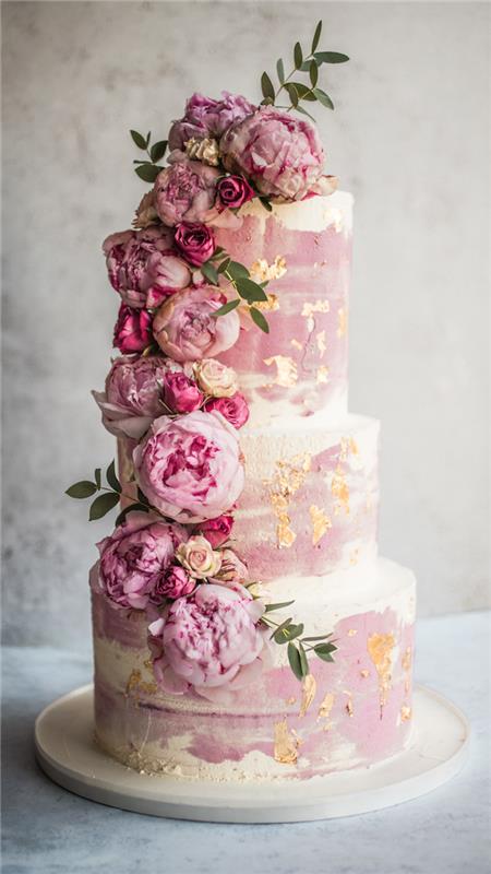 krans av färska rosa blommor för att dekorera bröllopstårta i rosa och vitt med enkla gyllene mönster