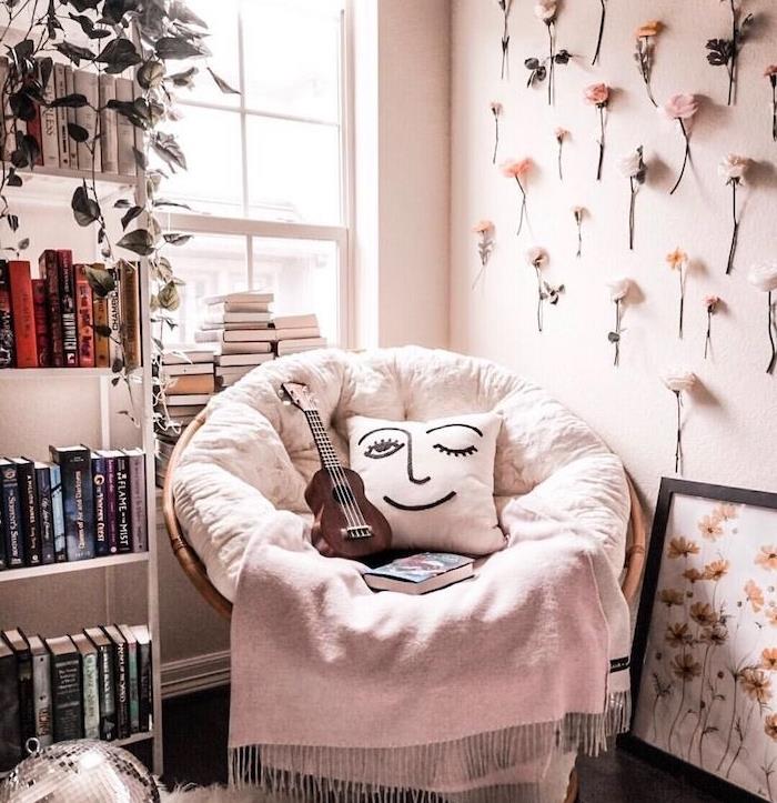 bekväm fåtölj för läsning med ljusgrå filt och ansikte kudde bokhylla vit skåpvägg dekorerad med färska blommor