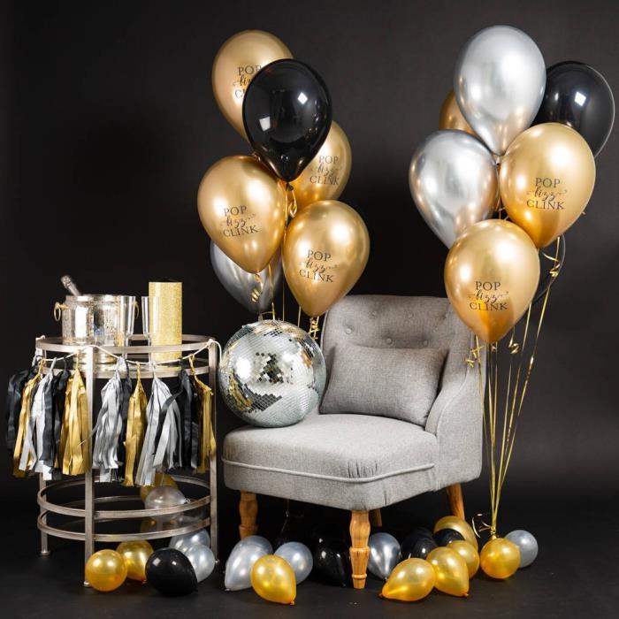 snygg svart och guld födelsedagsdekoration, fotobooth hörn med grå fåtölj och metallbord med heliumballongdekoration